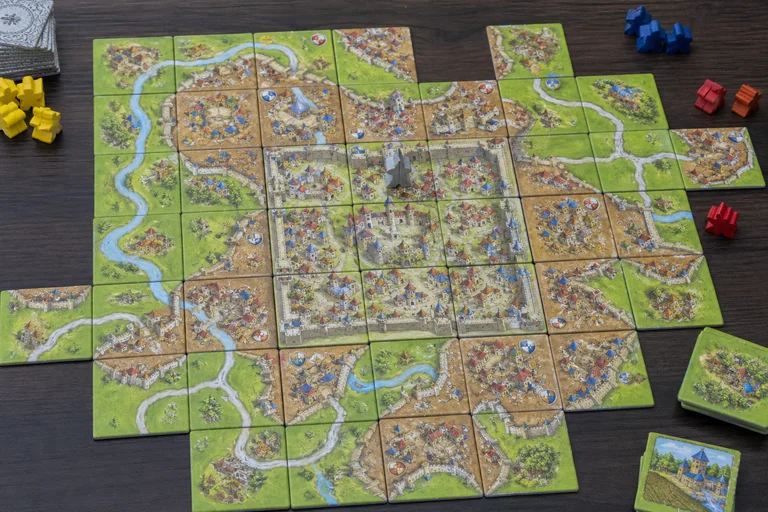 Mani che posizionano una tessera strada su Carcassonne